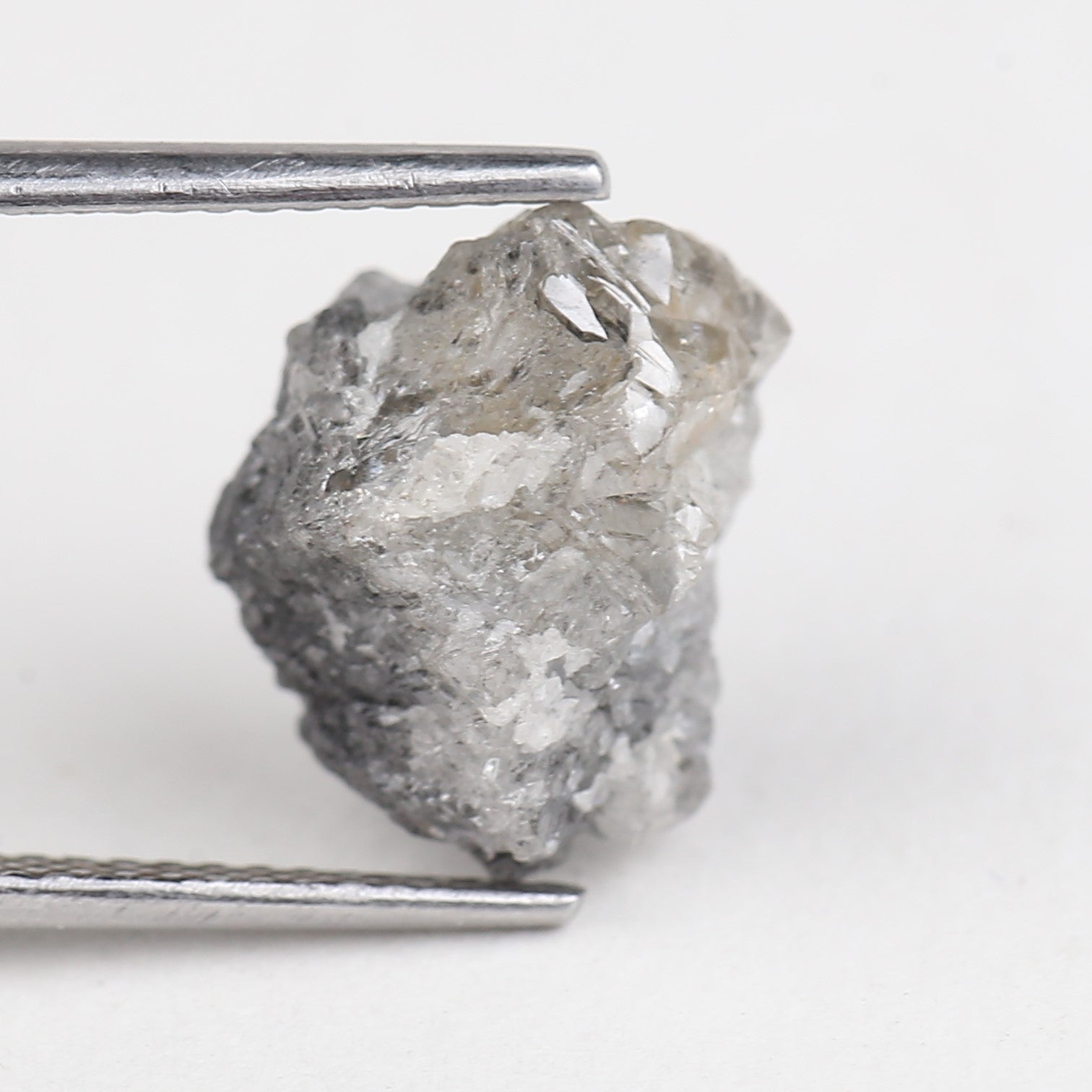Raw diamond held by tweezers on a white background