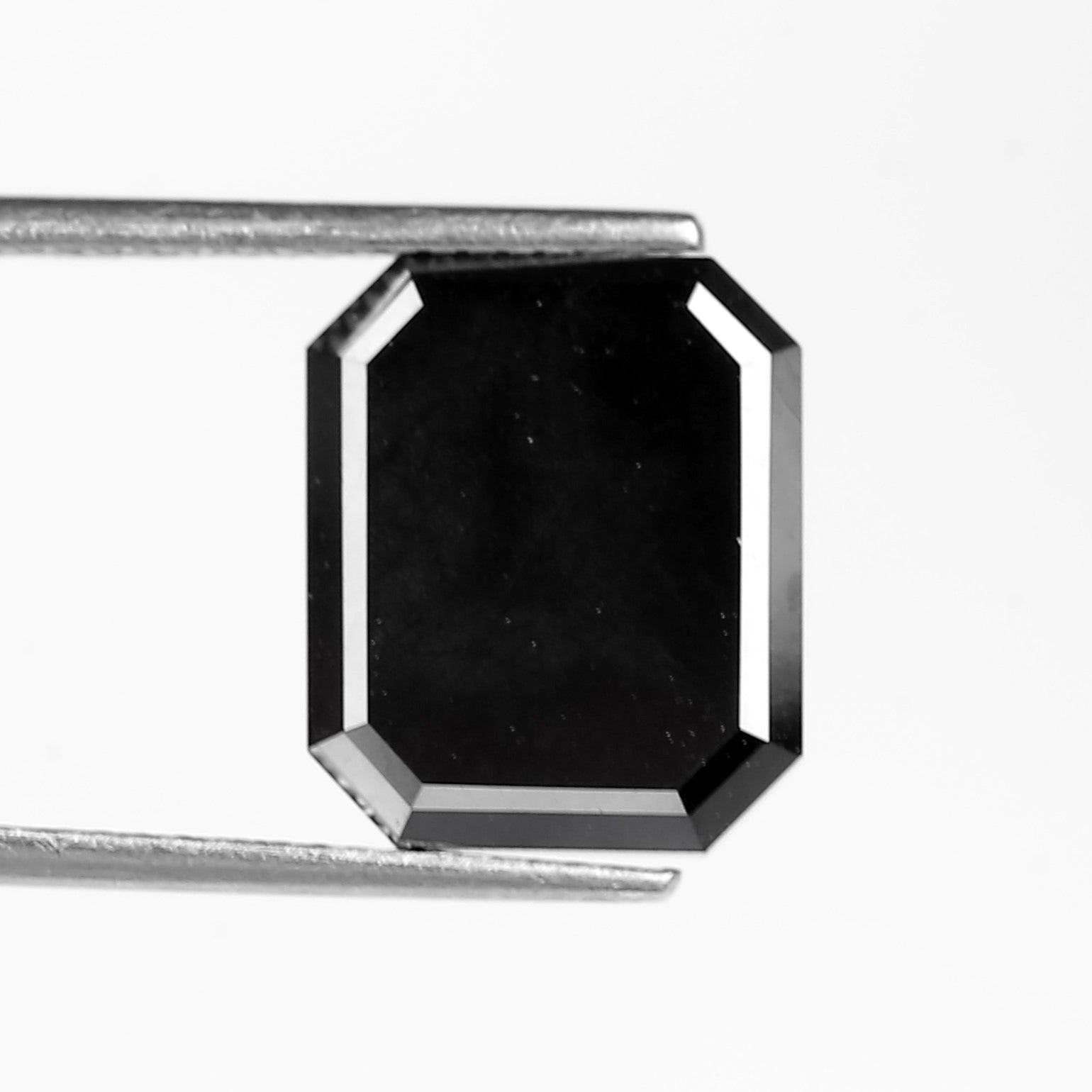 Black emerald diamond held by tweezers on a white background