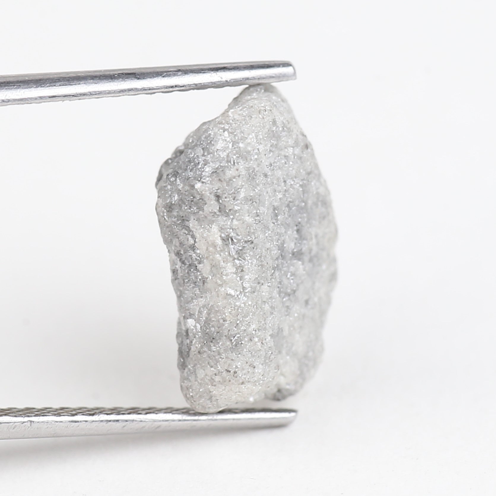 Raw diamond held by tweezers on a white background