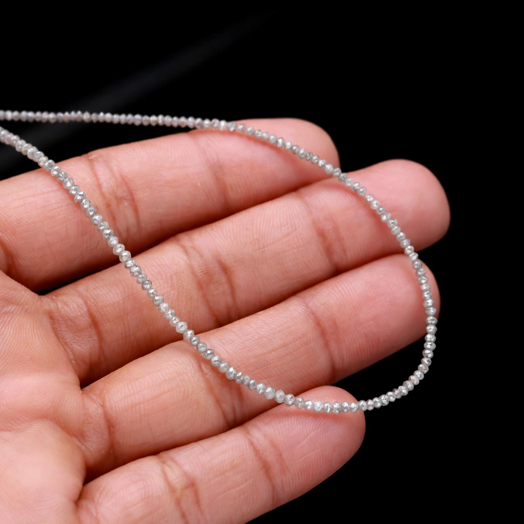 Thin string of small beads held between fingers against a black background