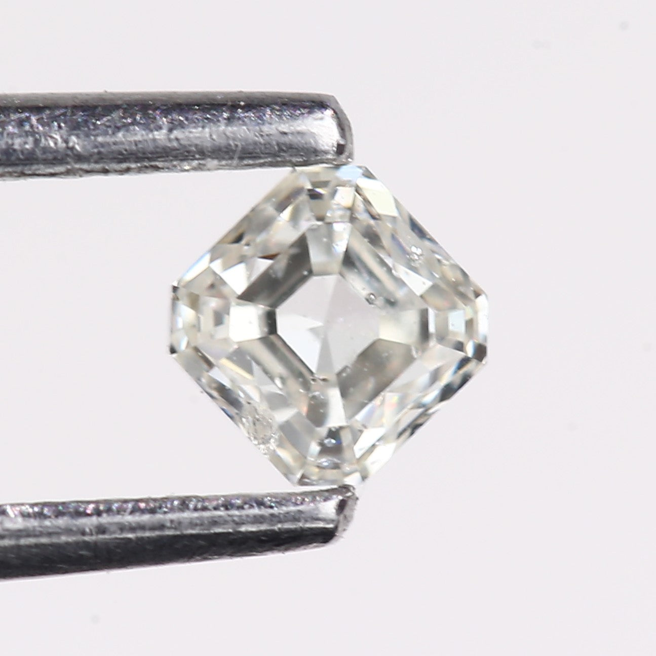 Natural hexagon step cut diamond held in tweezers, featuring a light champagne-white tone with clear faceting, geometric symmetry, and visible natural inclusions against a white background.