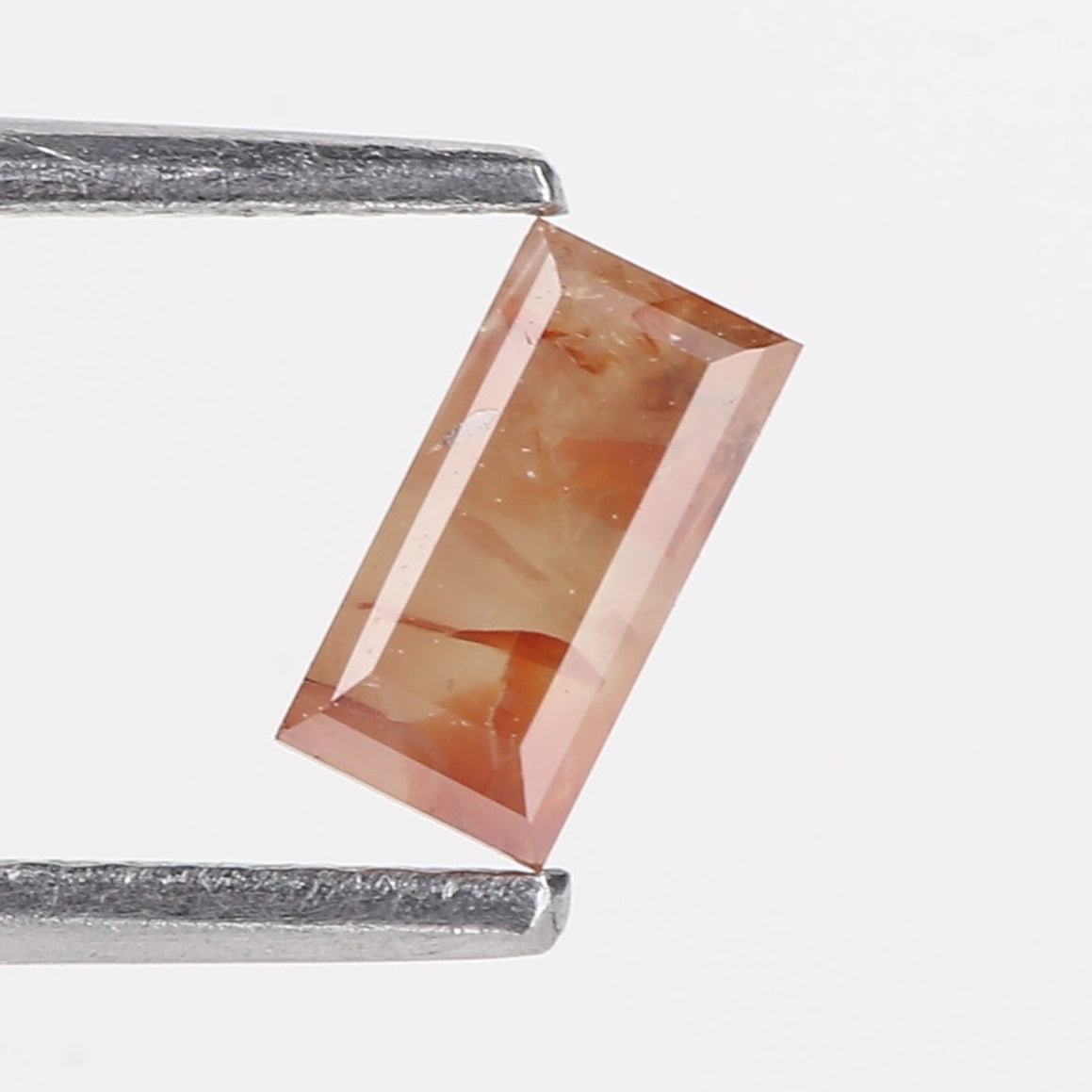Rectangular pink gemstone held between tweezers on a white background