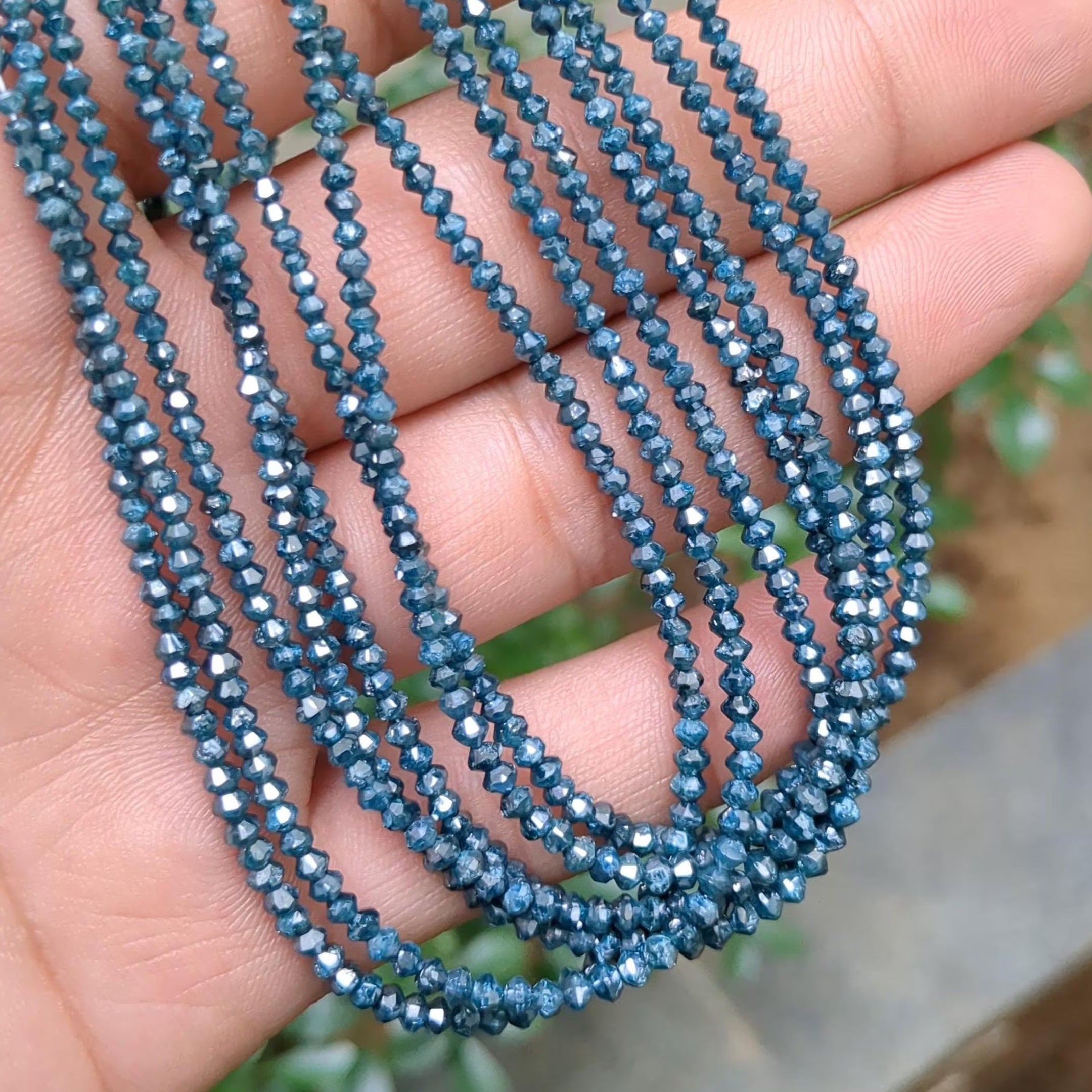 Blue beaded necklace held in a hand with a blurred natural background
