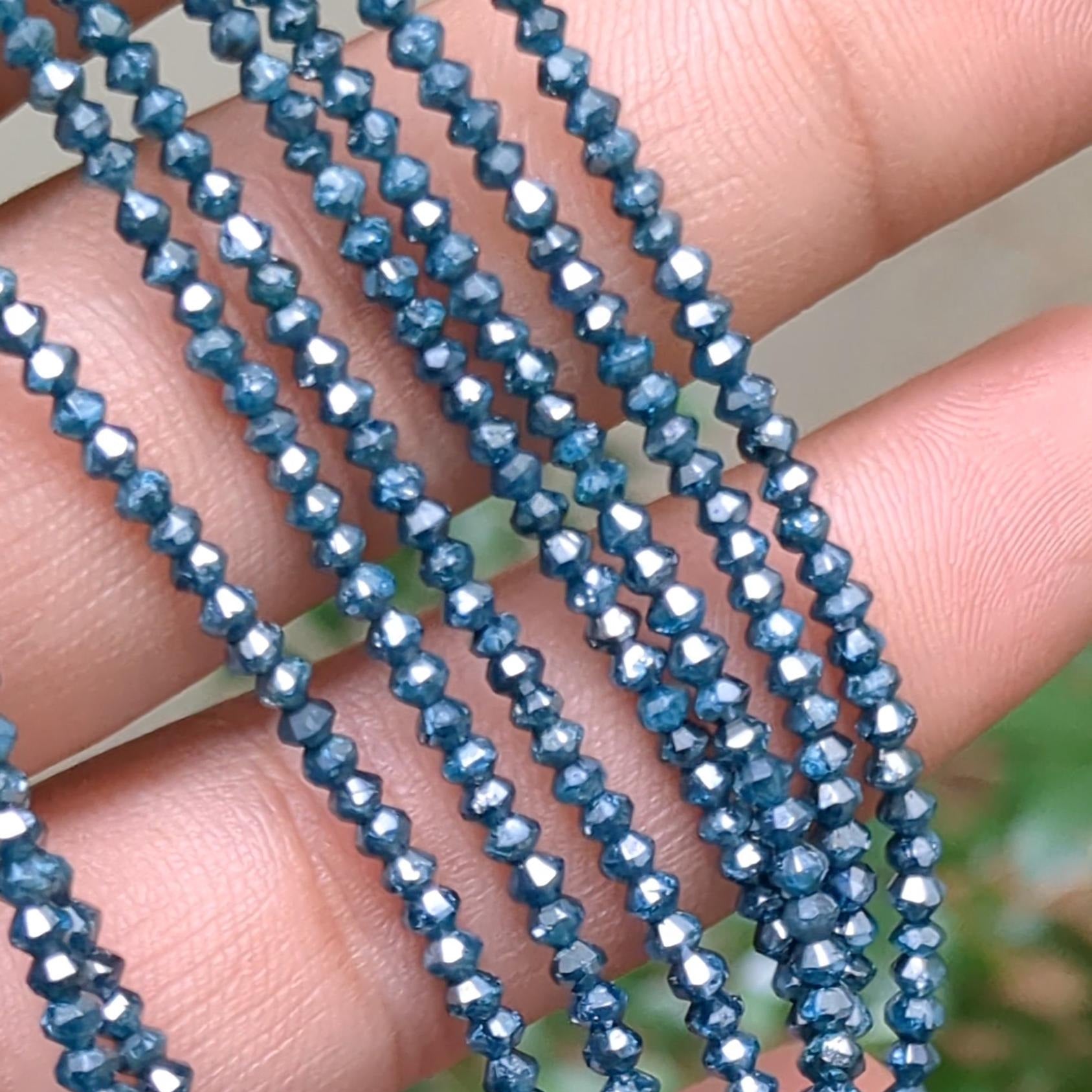 Close-up of blue beaded strings held between fingers with a blurred green background