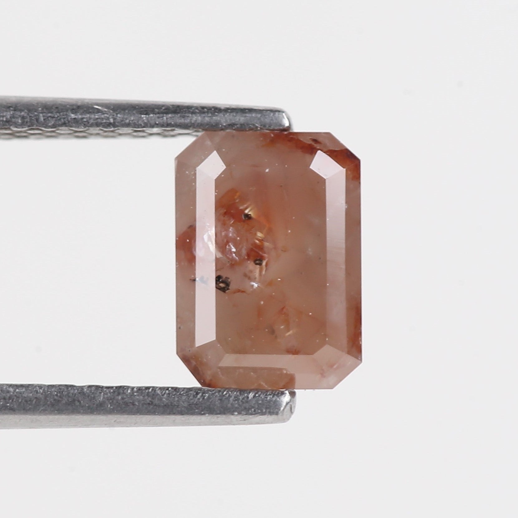 orange diamond held by tweezers on a light gray background