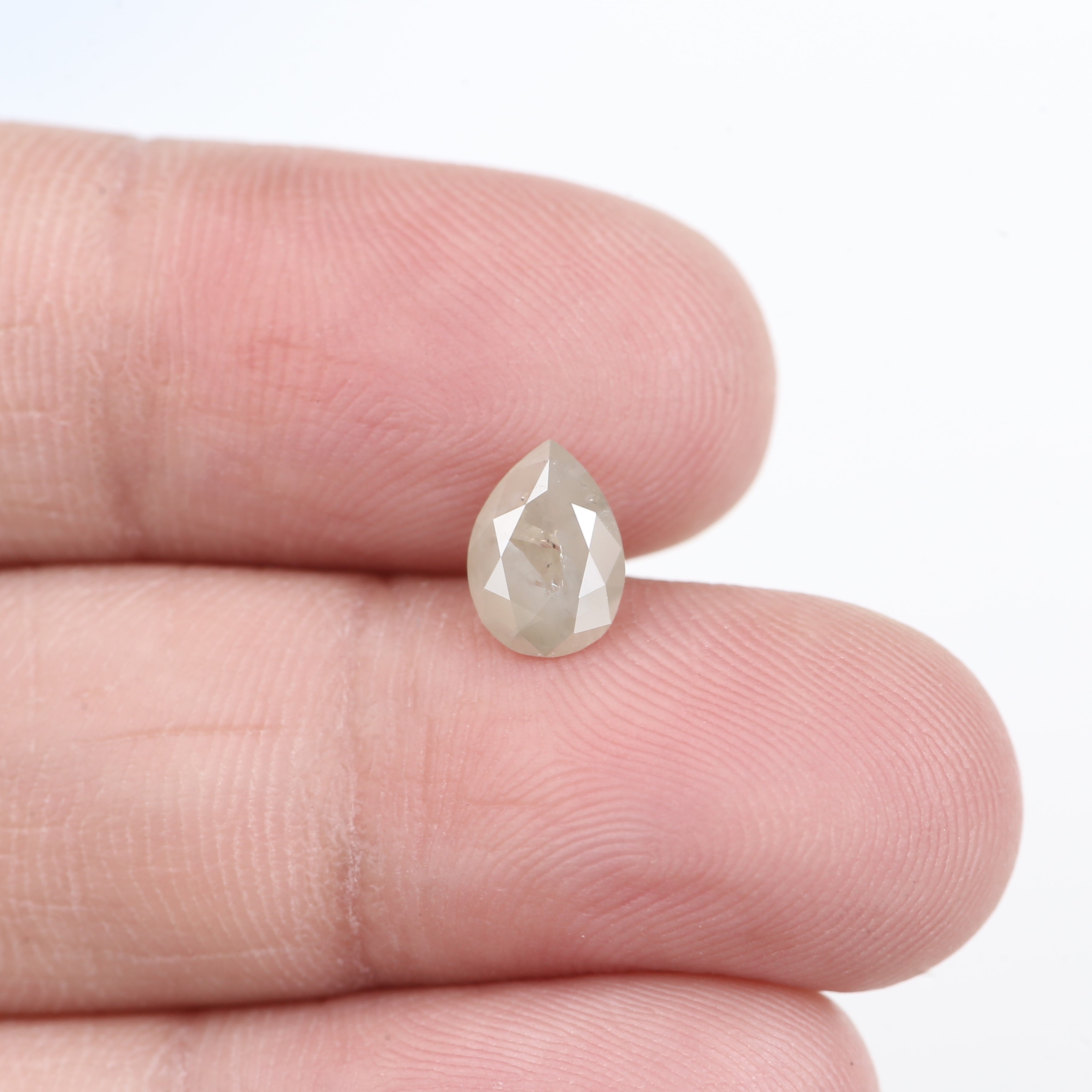 Teardrop-shaped diamond held between two fingers on a white background