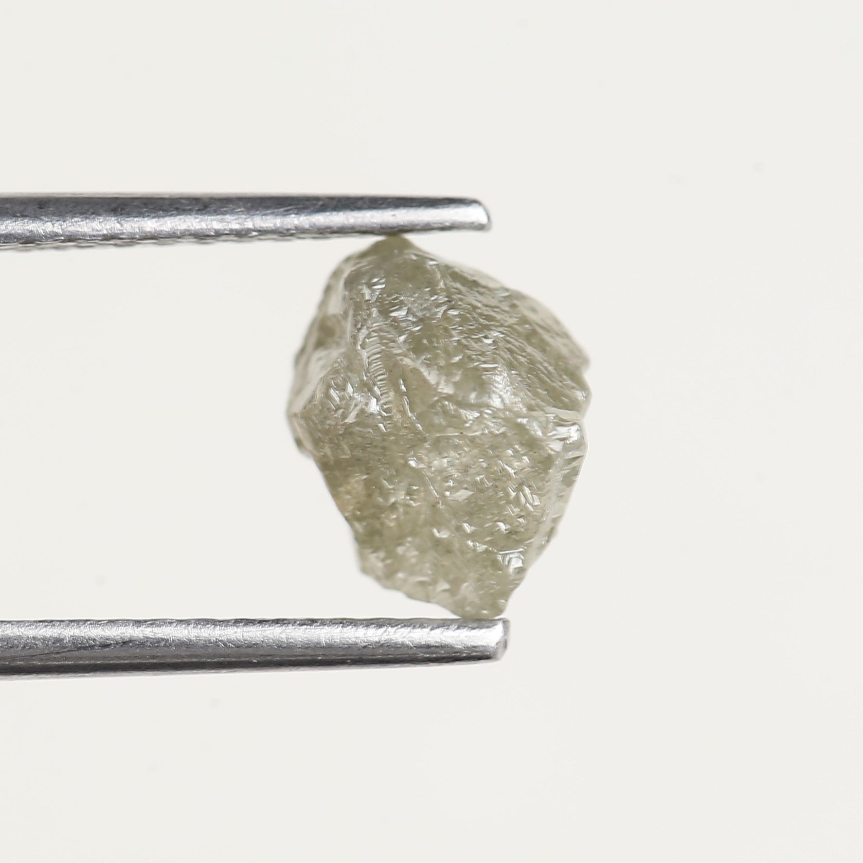 Raw diamond held by tweezers on a white background