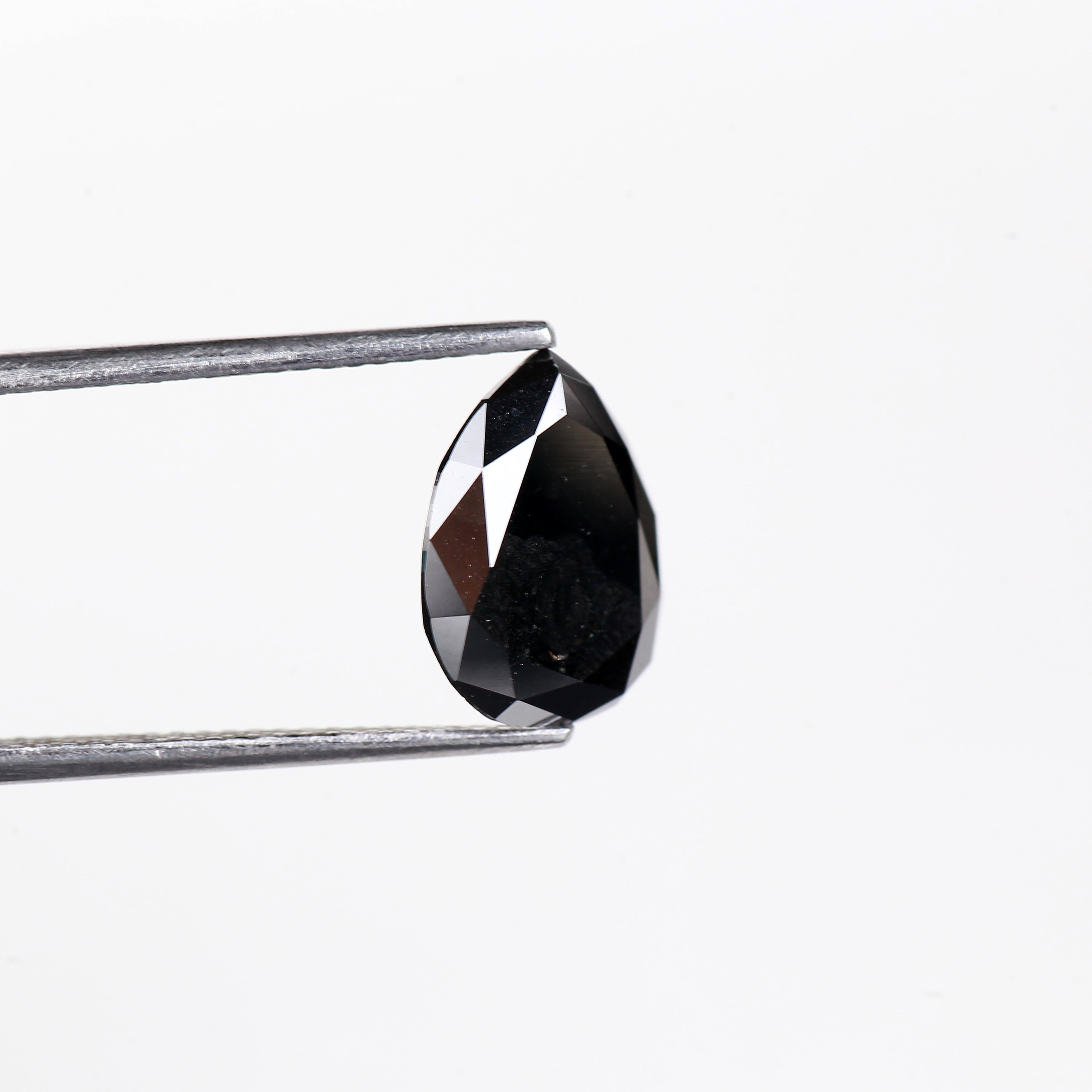 Teardrop-shaped black gemstone held by tweezers on a white background