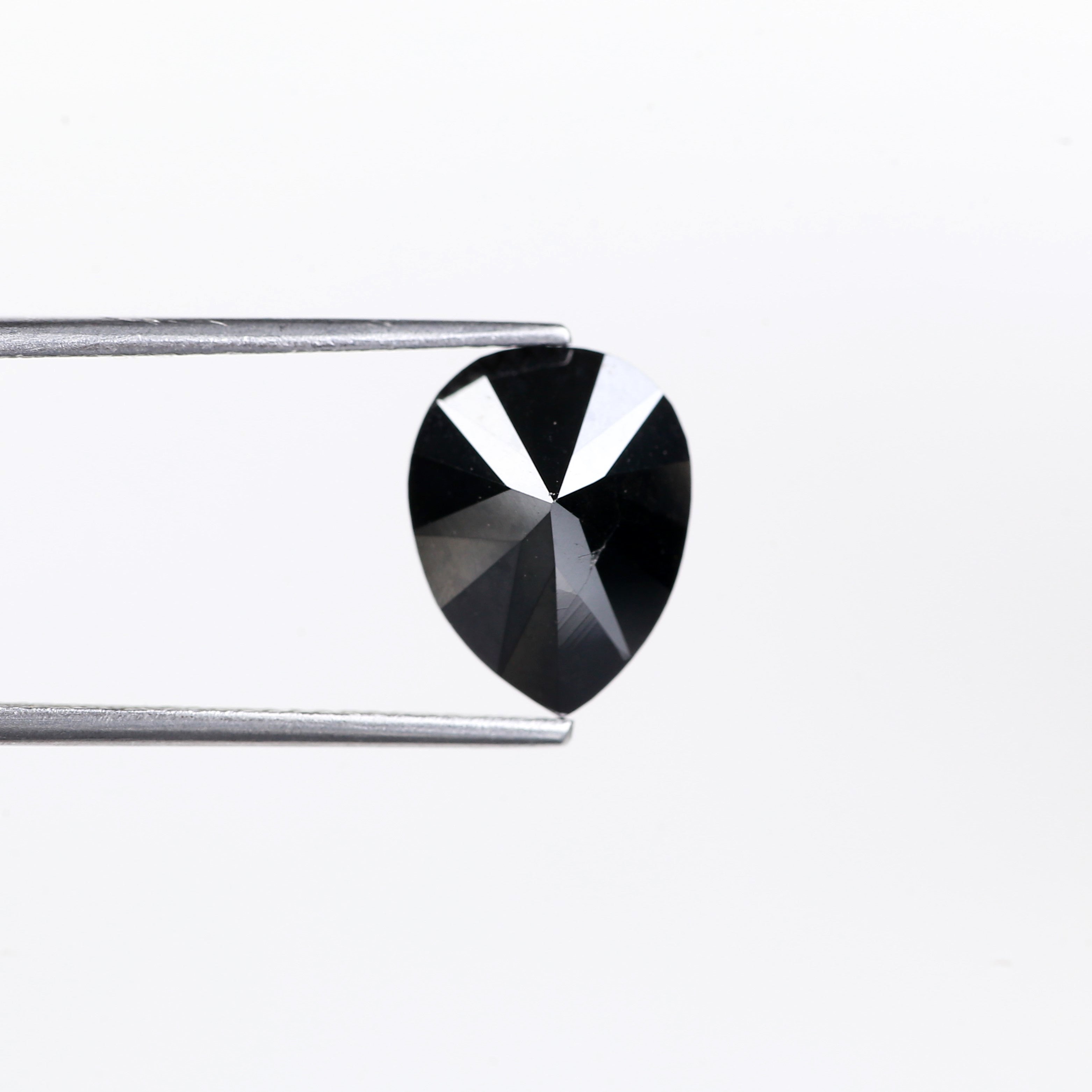 Heart-shaped black gemstone held by tweezers on a white background