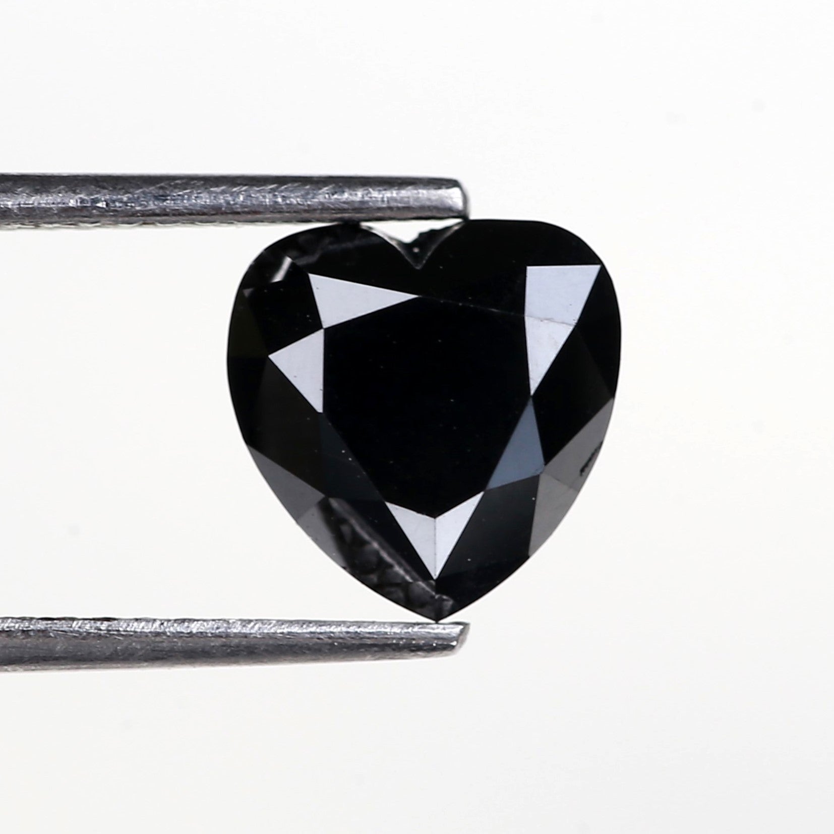 Heart-shaped black gemstone held between tweezers on a white background
