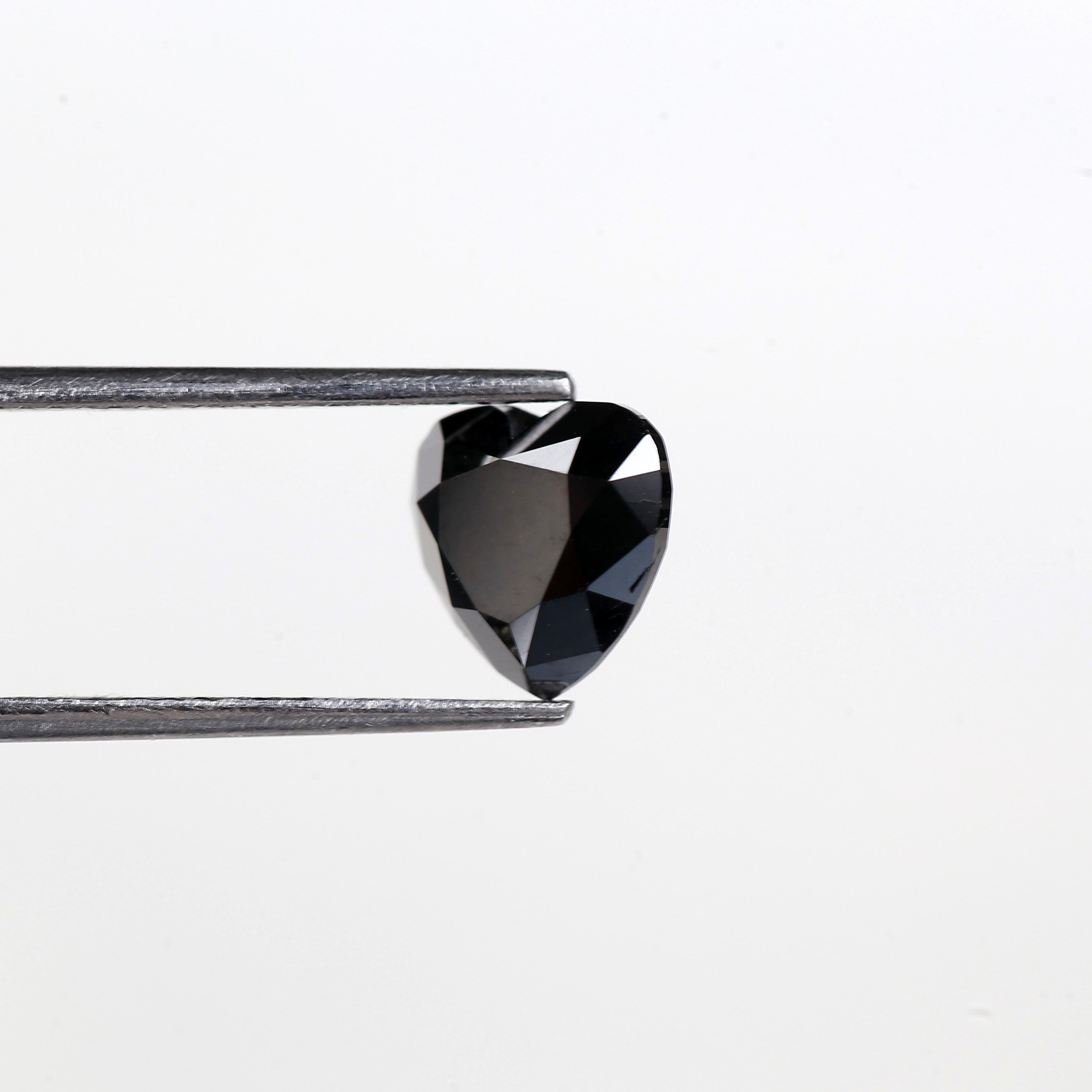Heart-shaped black diamond held by tweezers on a light gray background