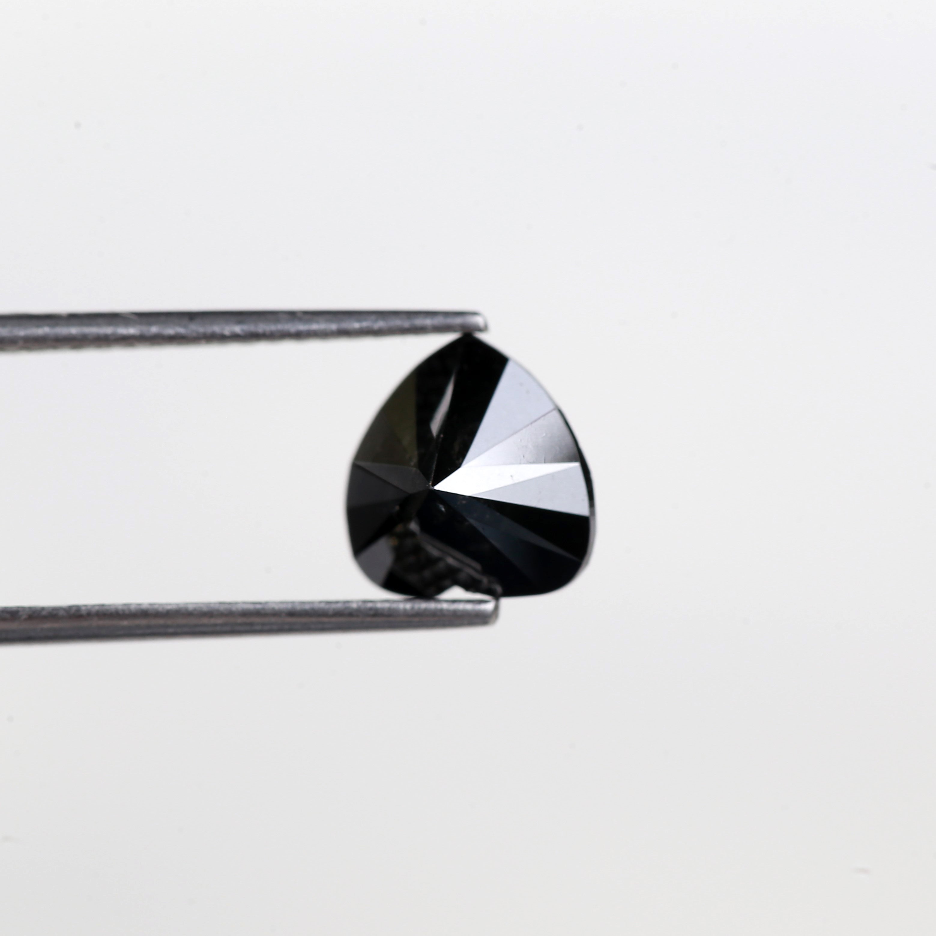 Teardrop-shaped black gemstone held by tweezers on a light gray background