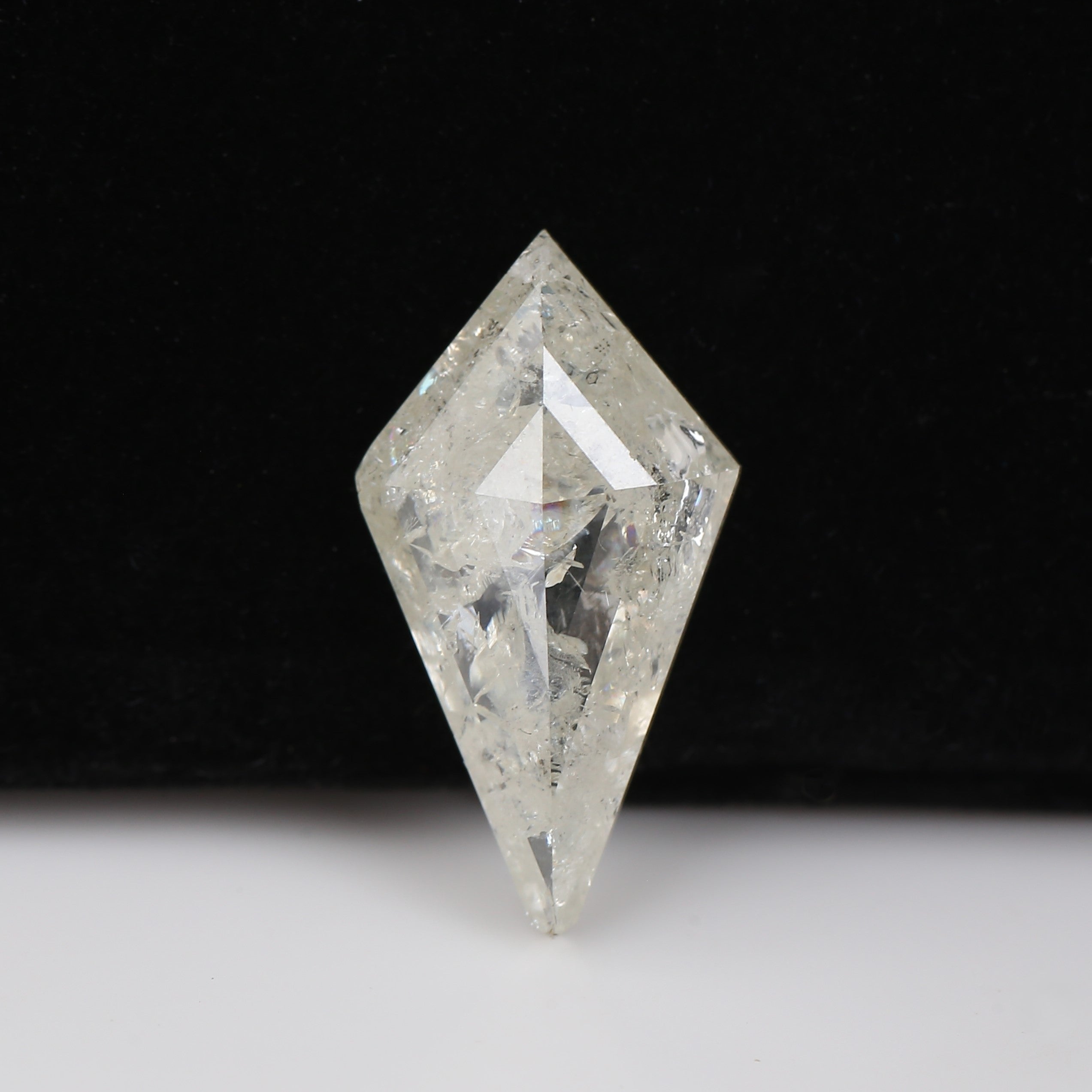A clear, faceted diamond-cut gemstone with internal inclusions, standing upright on a white surface against a solid black background.