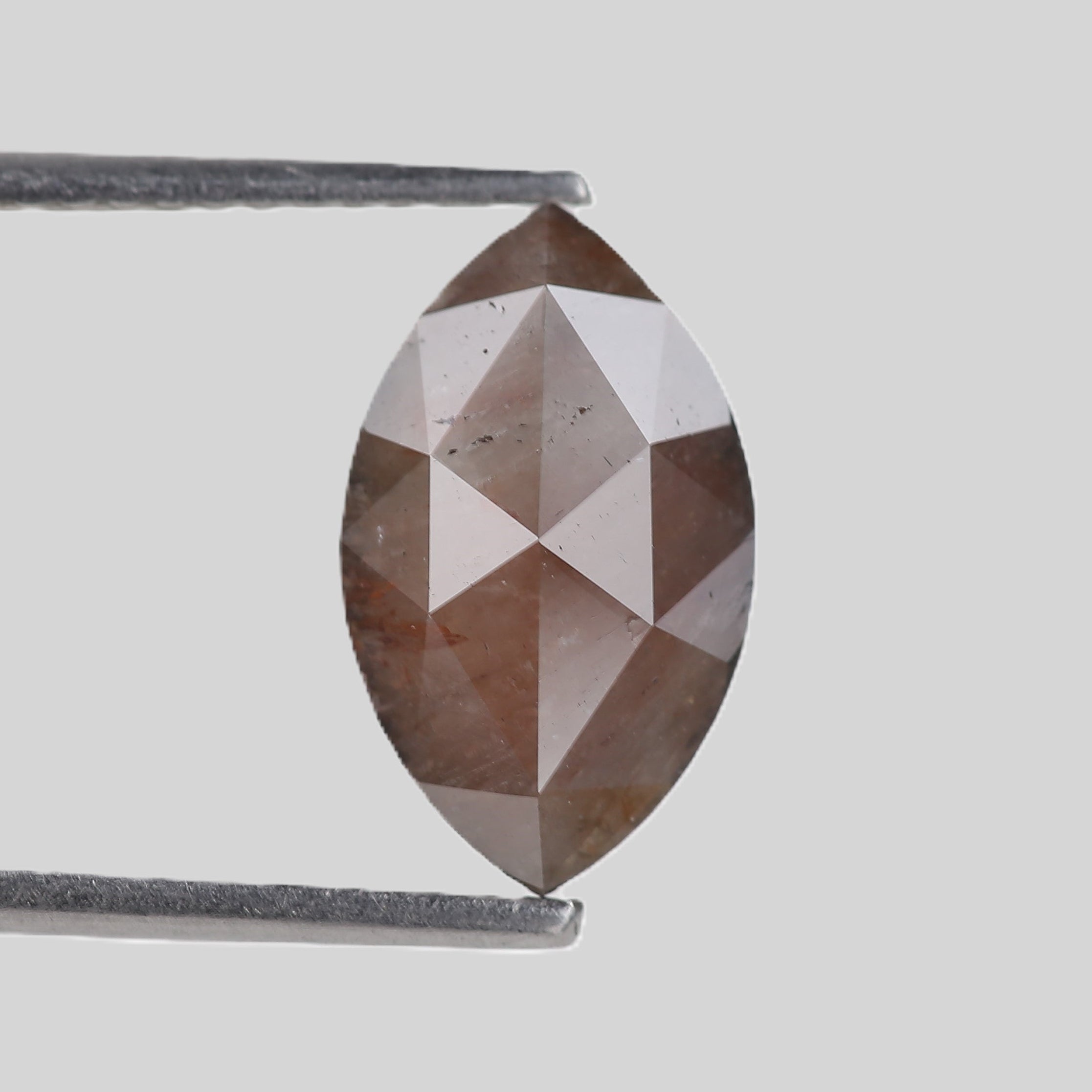 Faceted gemstone held by tweezers on a light gray background