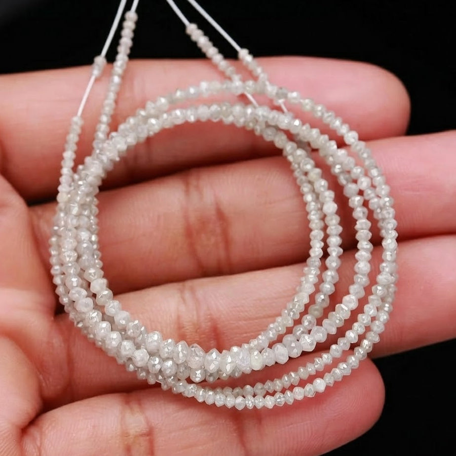Three strands of small white beads held in a hand against a black background