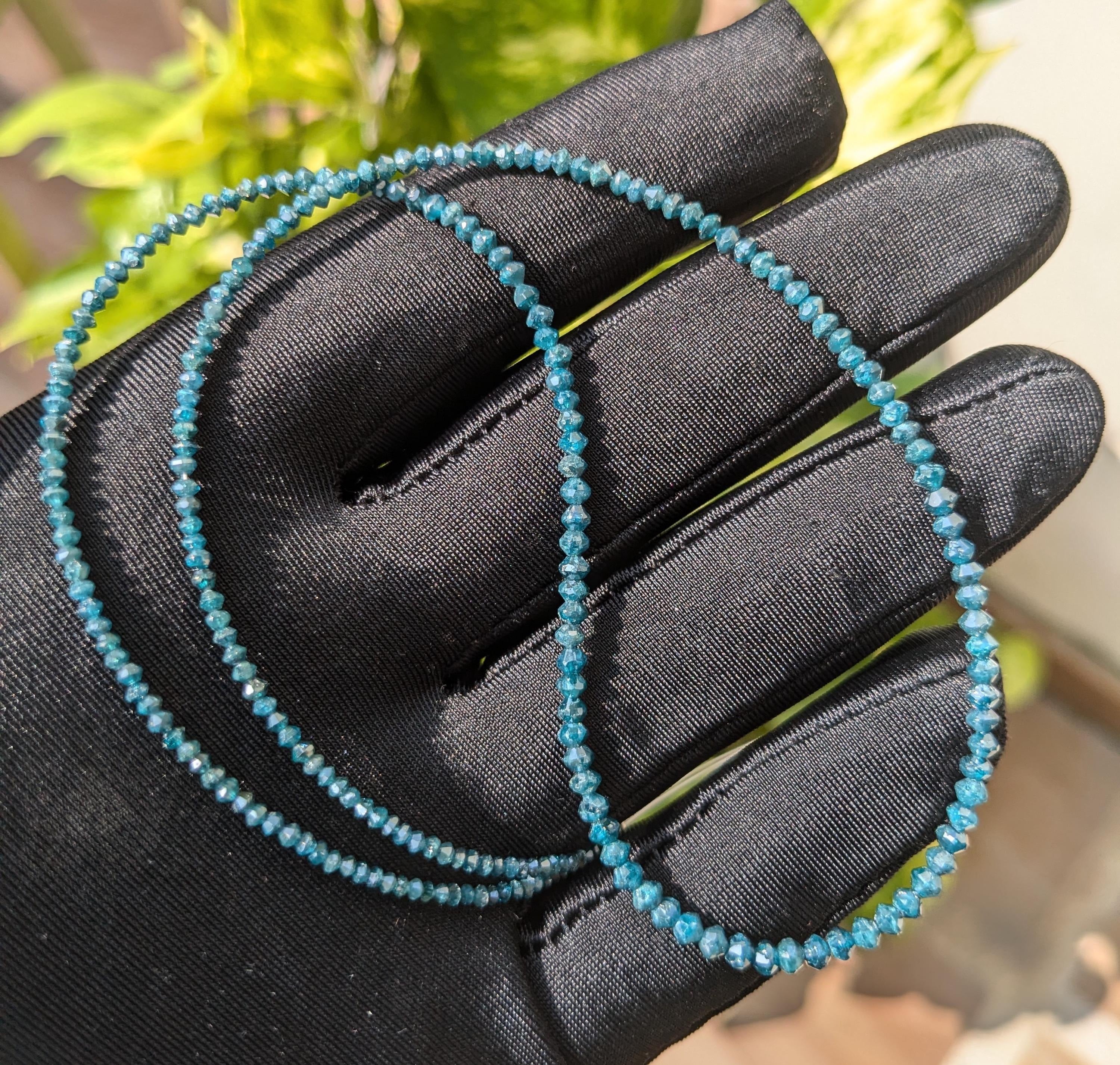 Turquoise beaded necklace held in a black gloved hand with a blurred green background