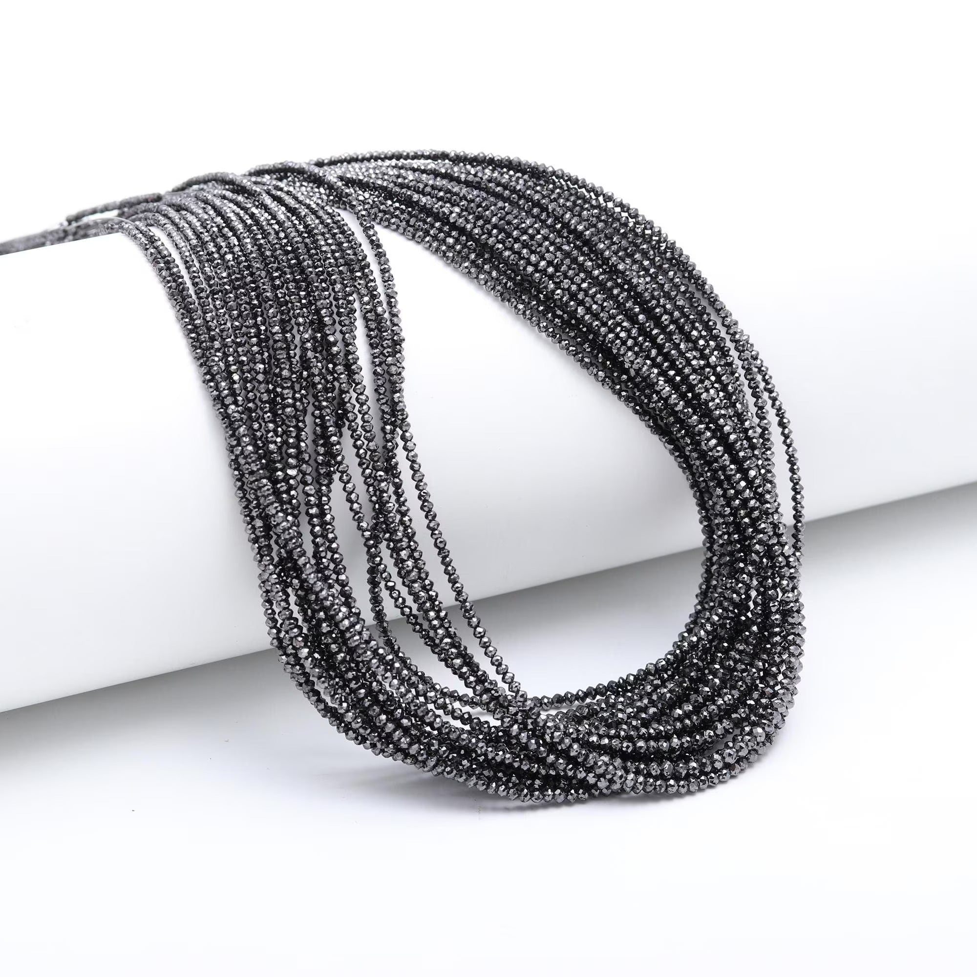 Multiple black beaded bracelets stacked on a white cylindrical object with a white background