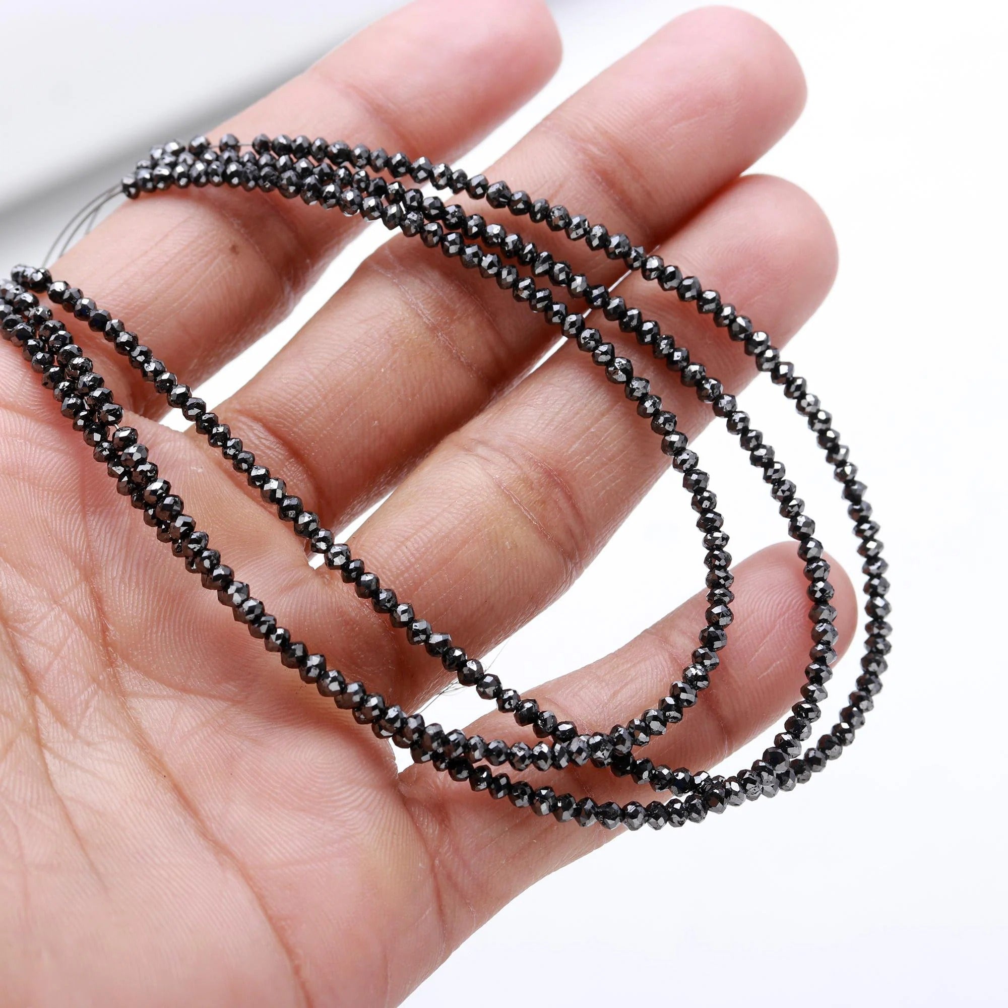 Black beaded necklace held in a hand against a white background