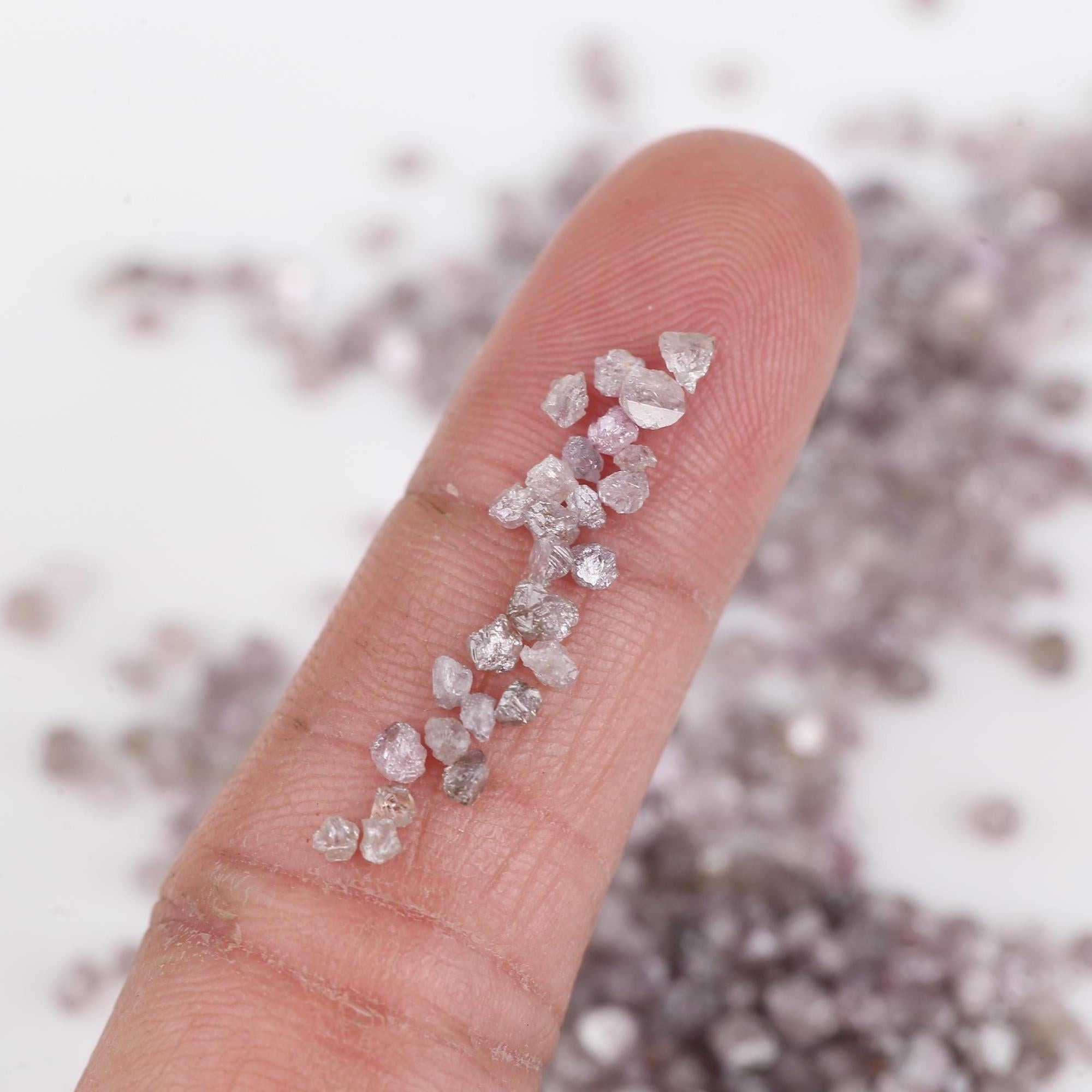 Raw diamonds on a person's finger with a blurred diamond background