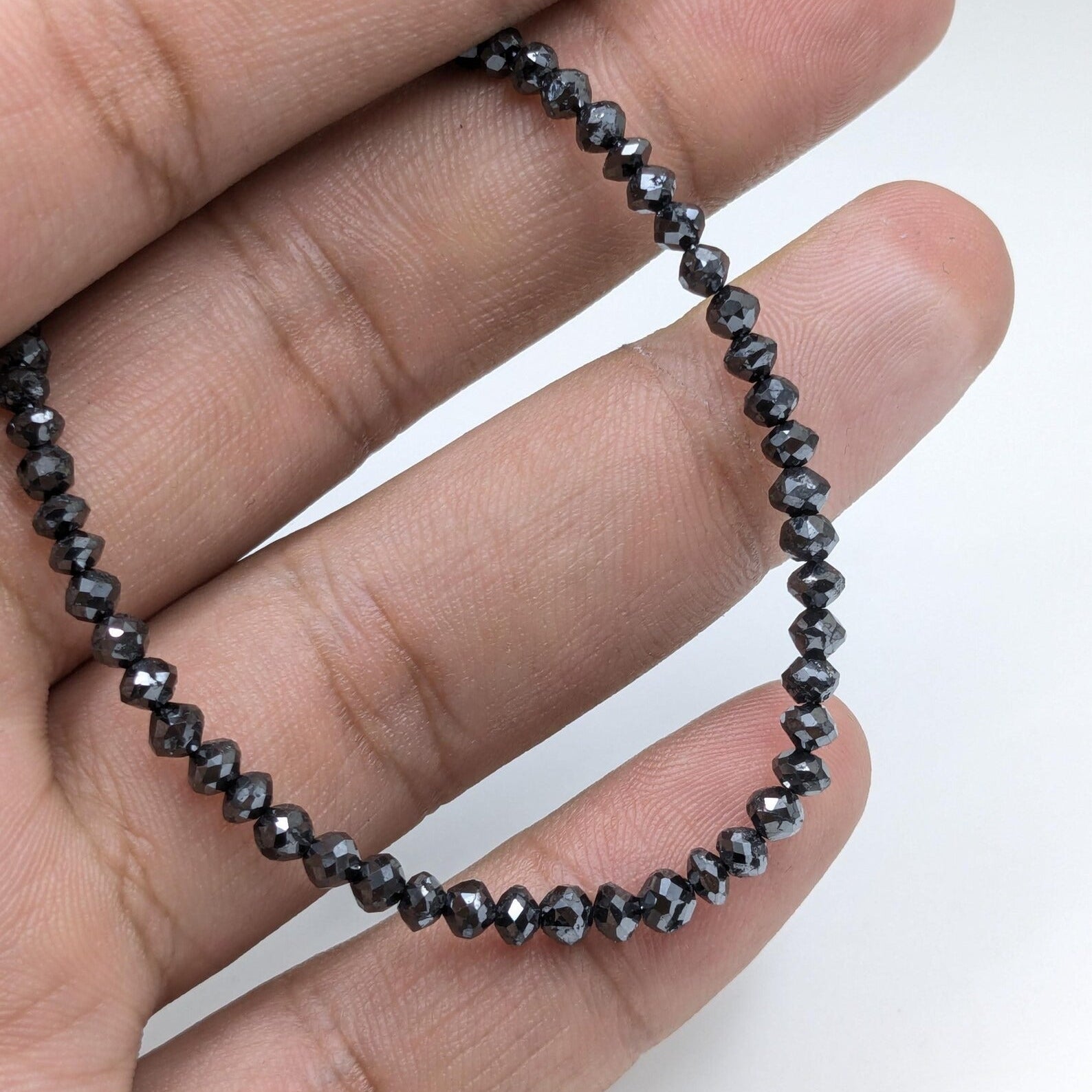 Hand holding a black beaded necklace against a white background