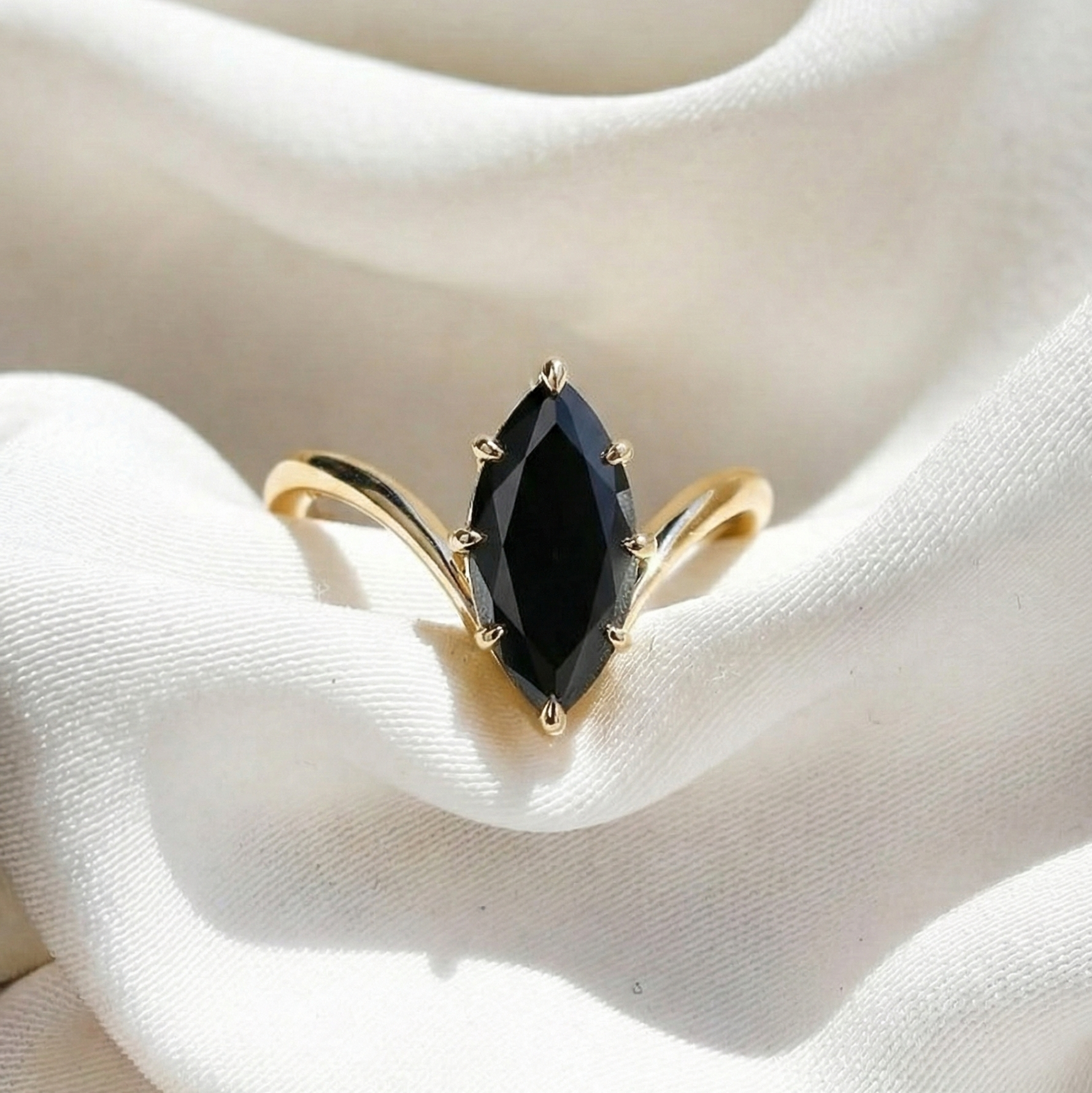 Gold ring with a black diamond on a white fabric background