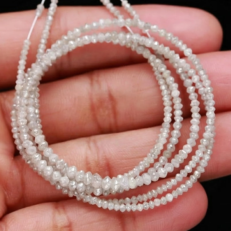 Three strands of small white beads held in a hand against a black background